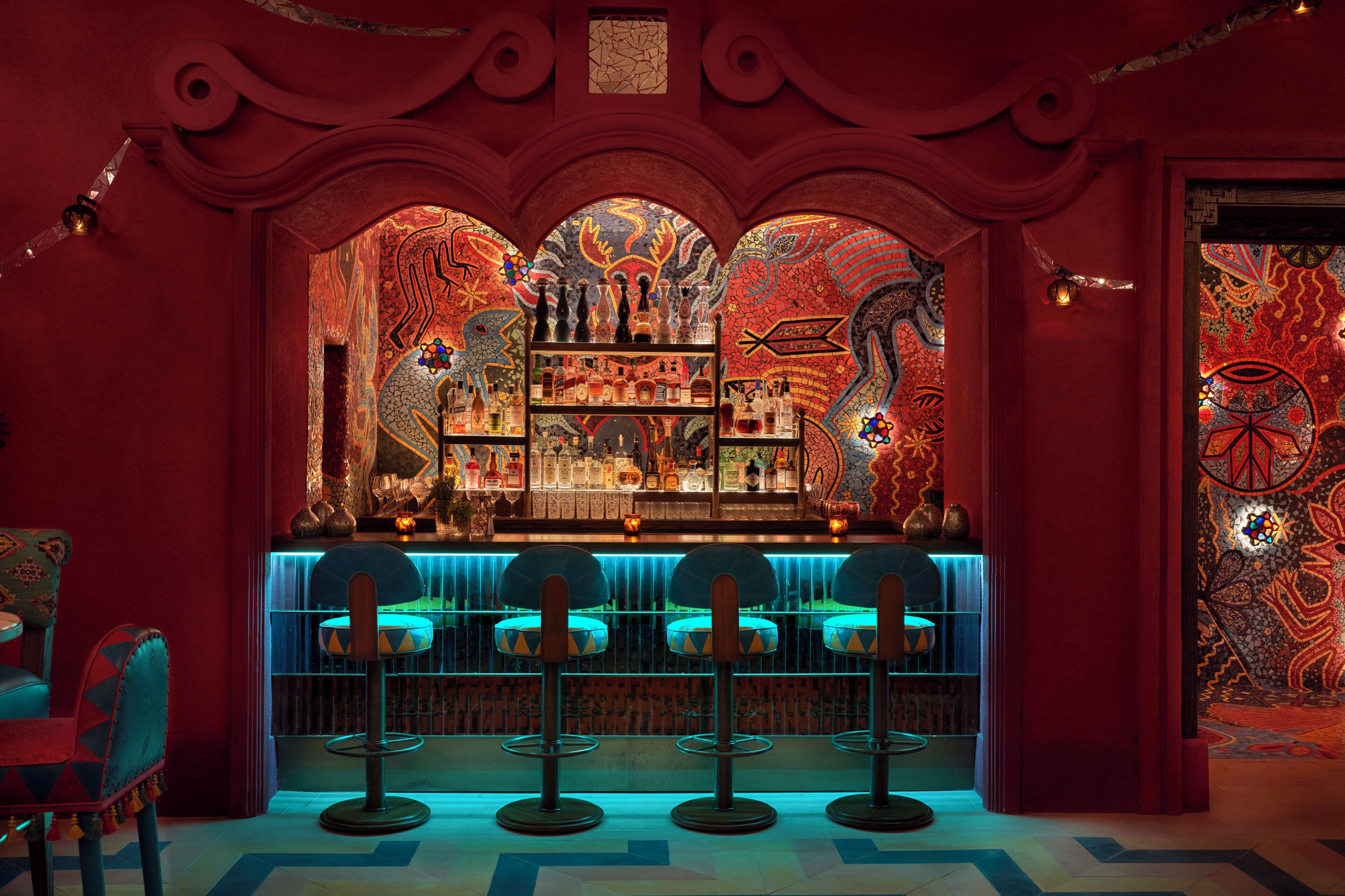 Zona de bar con decoración en rojo y azul, que incluye una barra y tres taburetes.