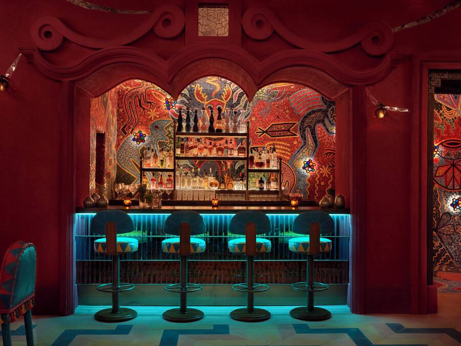 Zona de bar con decoración en rojo y azul, que incluye una barra y tres taburetes.