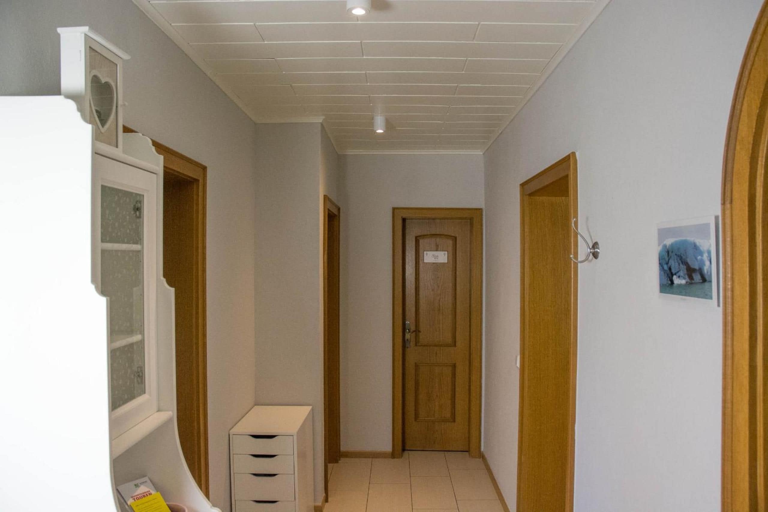 A narrow hallway with a wooden door at the end, a white cabinet with drawers, and a small picture on the wall.