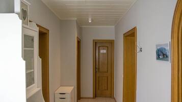 A narrow hallway with a wooden door at the end, a white cabinet with drawers, and a small picture on the wall.