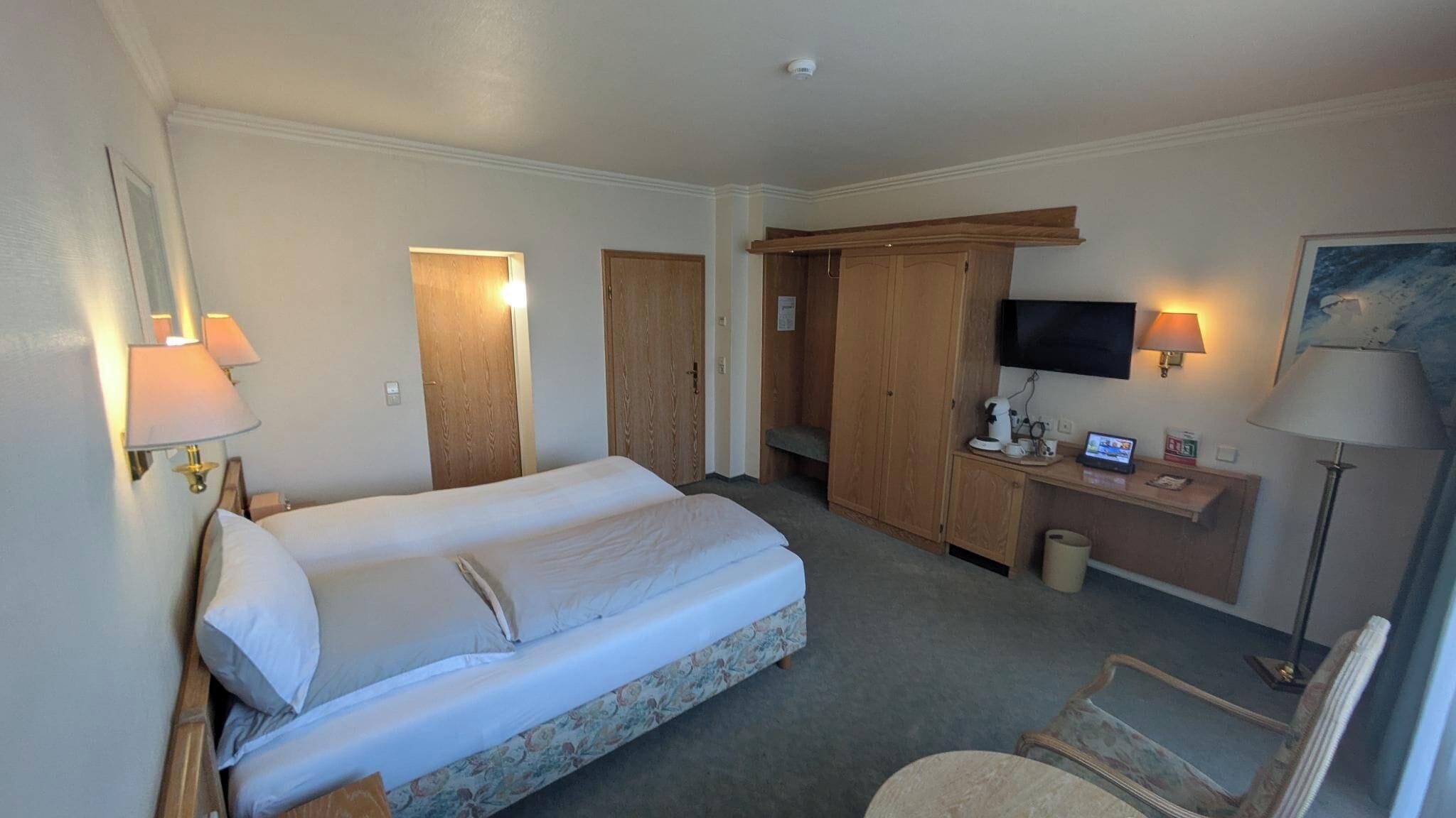 Une chambre d’hôtel avec un lit, un bureau avec un ordinateur, une télévision et une chaise.