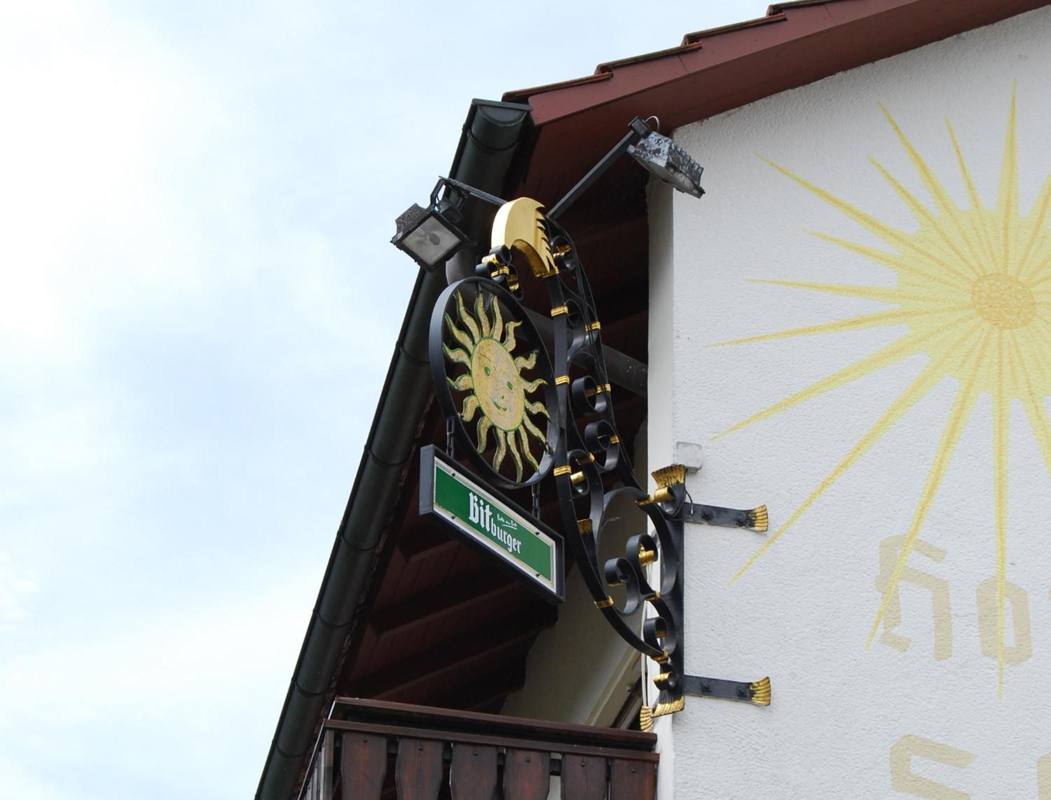 A building corner with a street sign for 'Bitburger' and a decorative sun motif on the wall.