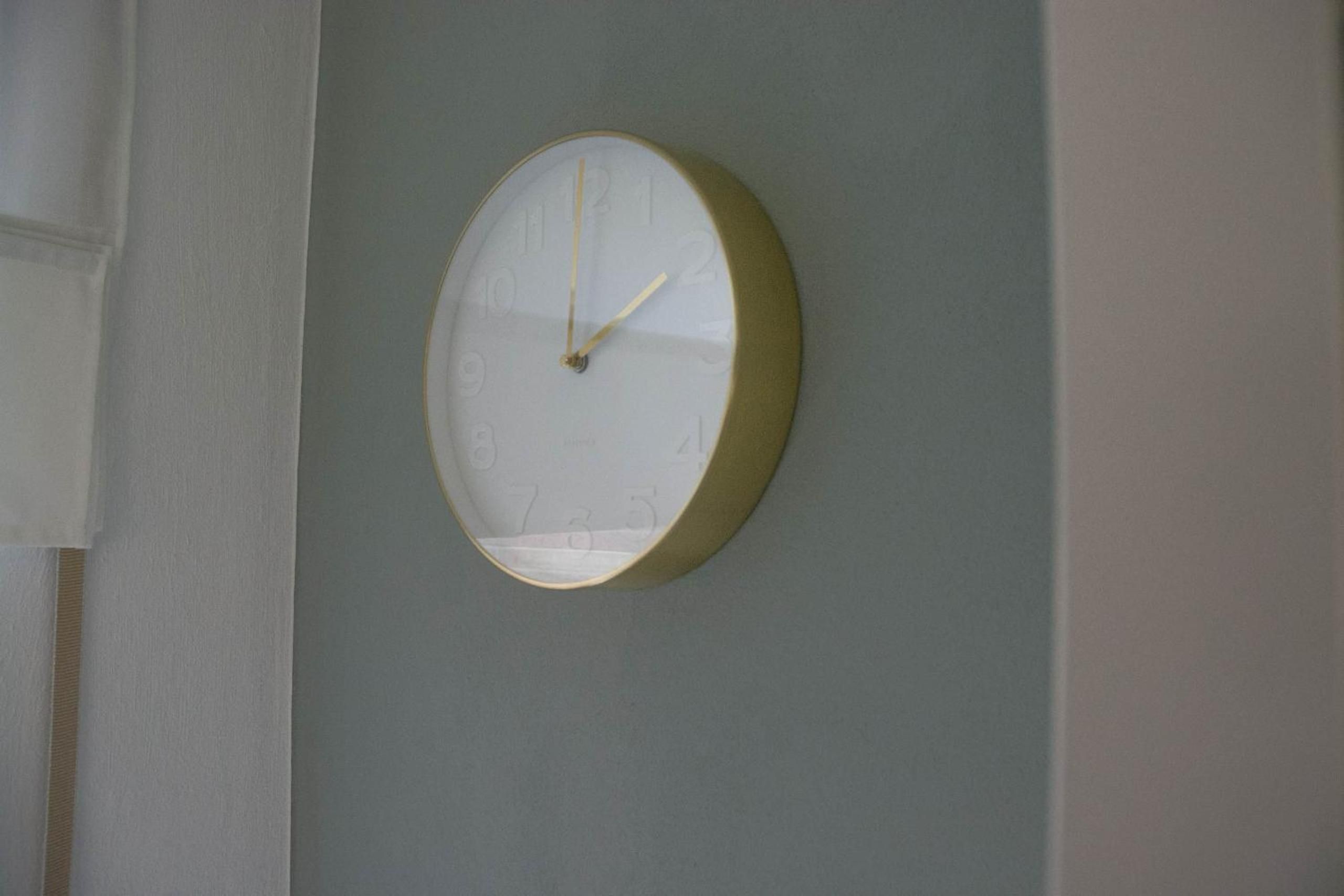 A round wall clock with a white face and gold trim, mounted on a light blue wall.