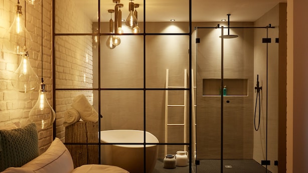 A modern bathroom with a glass shower enclosure, a white bathtub, and a wooden bench. - hotel friends Zeche Zollverein - Essen (Essen)