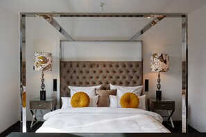 A modern bedroom with a tufted headboard, a glass bedside table, and two wall-mounted lamps.