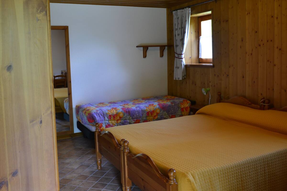 Een houten slaapkamer met een groot bed, een kleiner bed en een houten kledingkast.