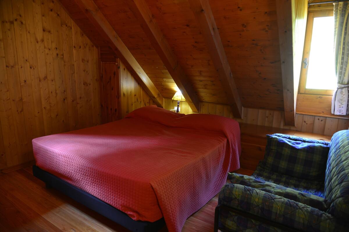Een houten kamer met een bed, een stoel en een raam.