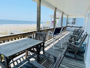 A wooden deck with tables and chairs overlooking the beach.