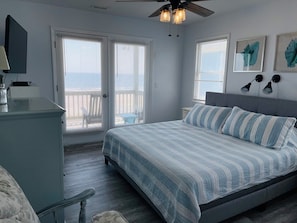 A bedroom with a bed, a desk, a chair, a ceiling fan, and two windows with blinds.