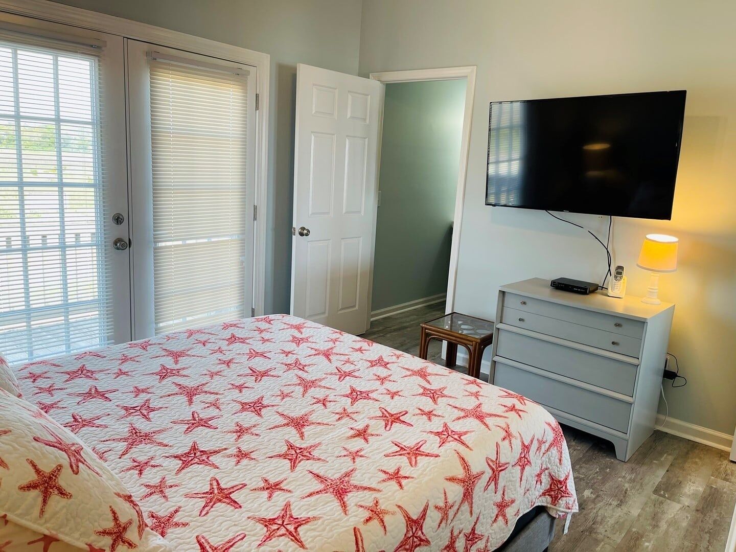 Un dormitorio con cama, televisor, lámpara y cómoda.