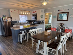 A modern kitchen with a central island, white cabinetry, and a dining area with a wooden table and white chairs.