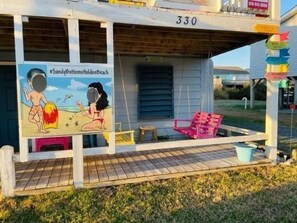 A beach-themed exterior with a porch, a swing chair, and a sign reading "SandyBottomsHoldenBeach". - Sandy Bottoms 4 Bedroom Home by RedAwning (Supply)