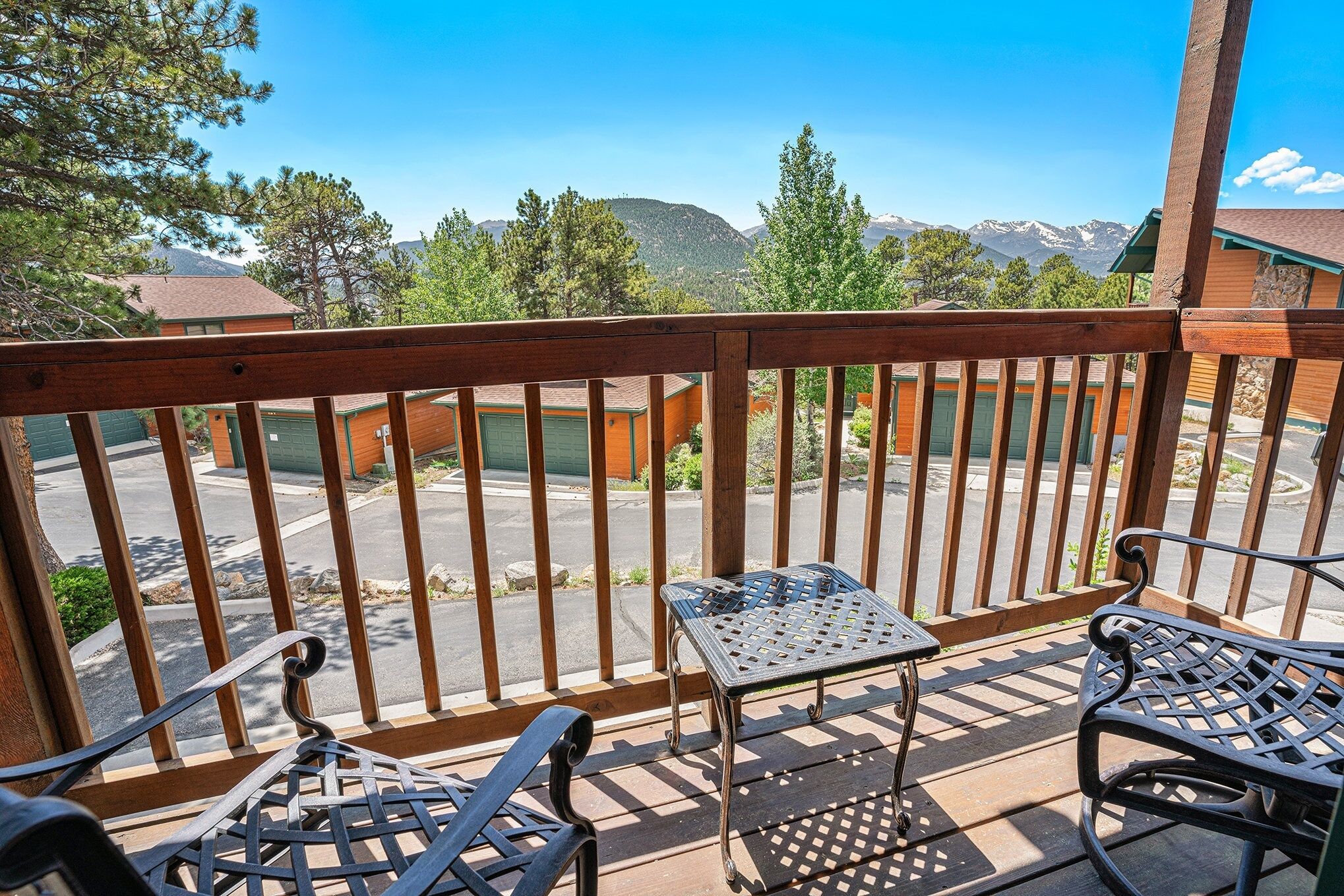 A balcony with a wooden railing, two metal chairs, and a small table.