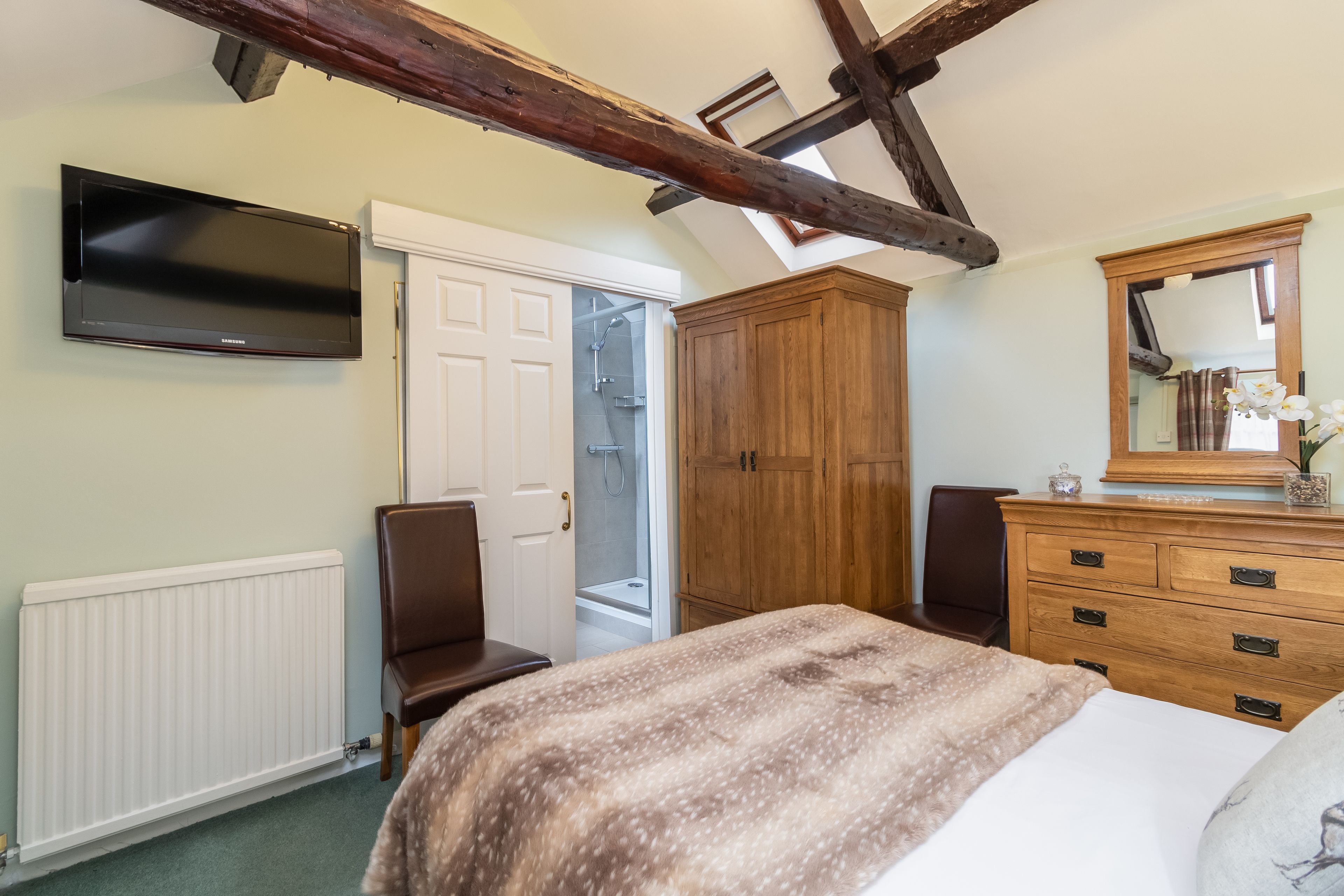 A bedroom with a bed, a wooden wardrobe, a television, and a bathroom door.