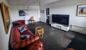 Una sala de estar con un televisor de pantalla plana grande, un sofá de cuero rojo, un sillón de mimbre y una mesita.