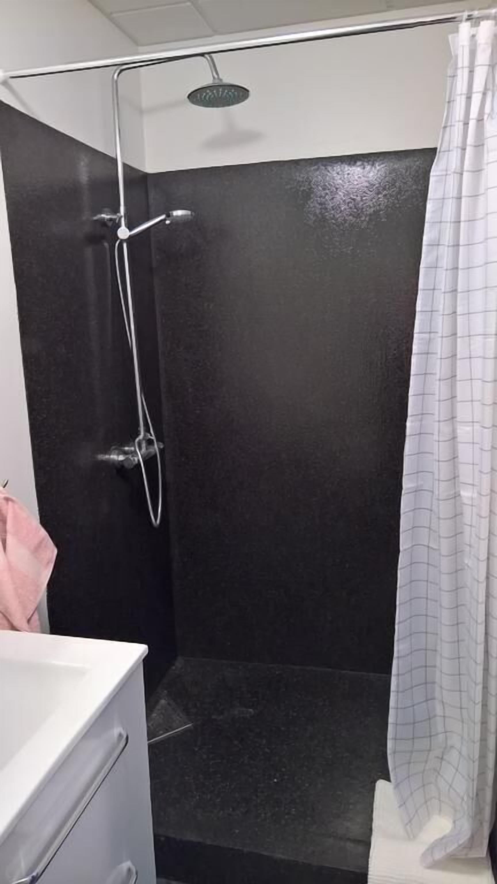 Un espace douche avec un mur noir, une pomme de douche et un rideau.