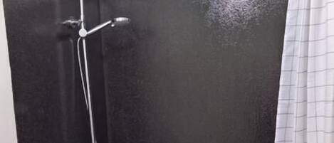 Un espace douche avec un mur noir, une pomme de douche et un rideau.