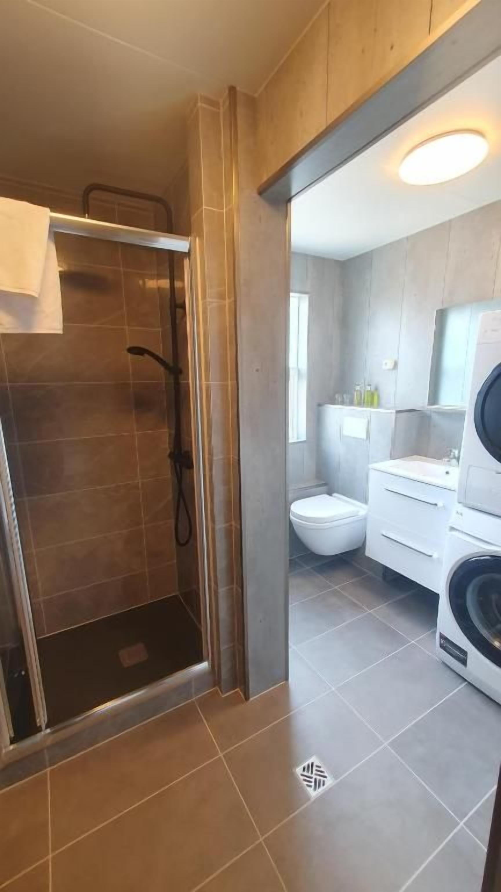 A modern bathroom with a shower, toilet, and washing machine.