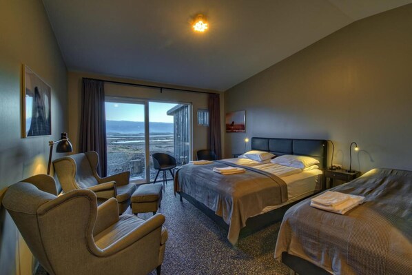 Habitación de hotel con dos camas, un escritorio, una silla y un ventanal con vistas al paisaje.