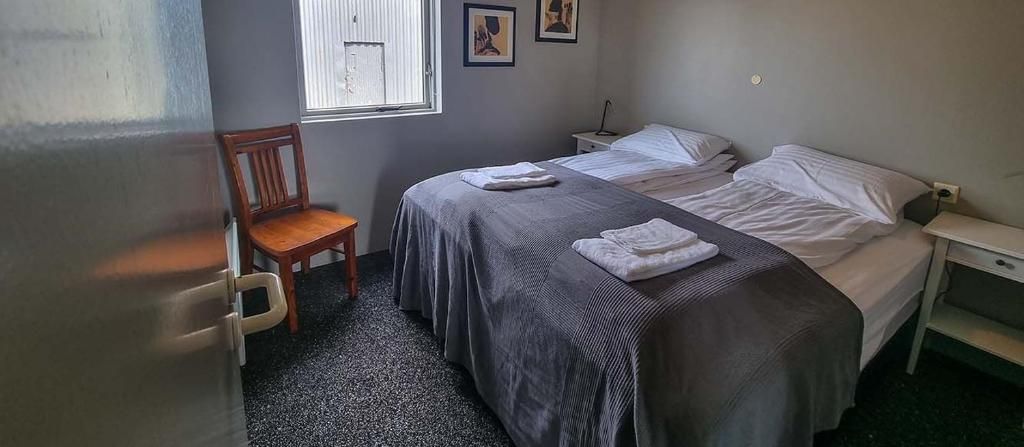 Una camera d'albergo con due letti, una sedia, un tavolino e una finestra.