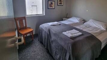 Una camera d'albergo con due letti, una sedia, un tavolino e una finestra.