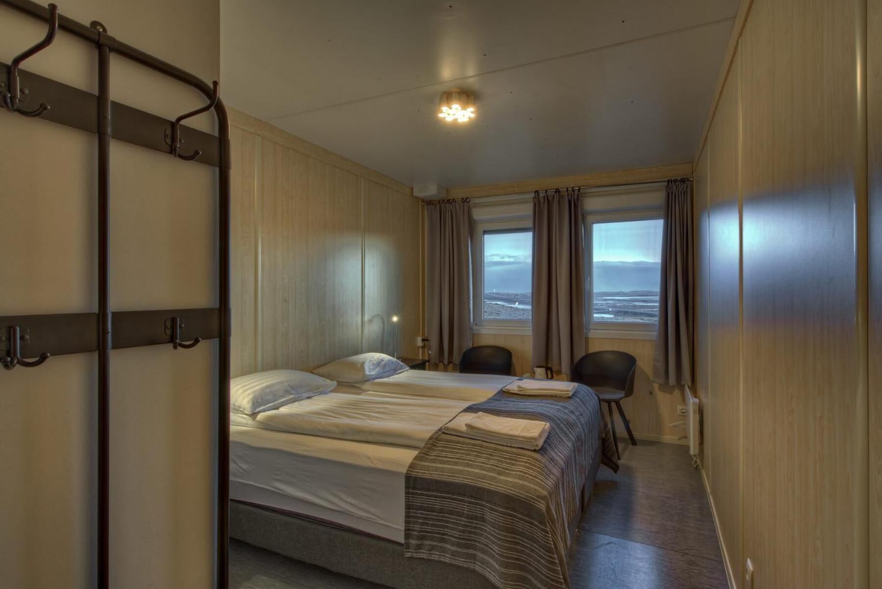 A hotel room with two beds, a desk, chairs, and a view of the sea.