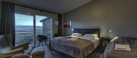 A hotel room with a large bed, two bedside tables, a chair, and a view of the beach.