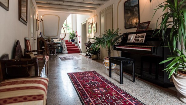 Un vaste salon agrémenté d’un magnifique piano à queue, d’une moquette rouge et d’un escalier menant à un autre niveau.