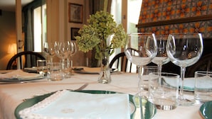 Une table à manger dressée avec des assiettes, des couverts et des verres à vin, et un vase de fleurs placé au centre.