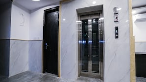 Un ascenseur moderne doté d’un écran numérique, d’une porte noire et de murs en marbre.