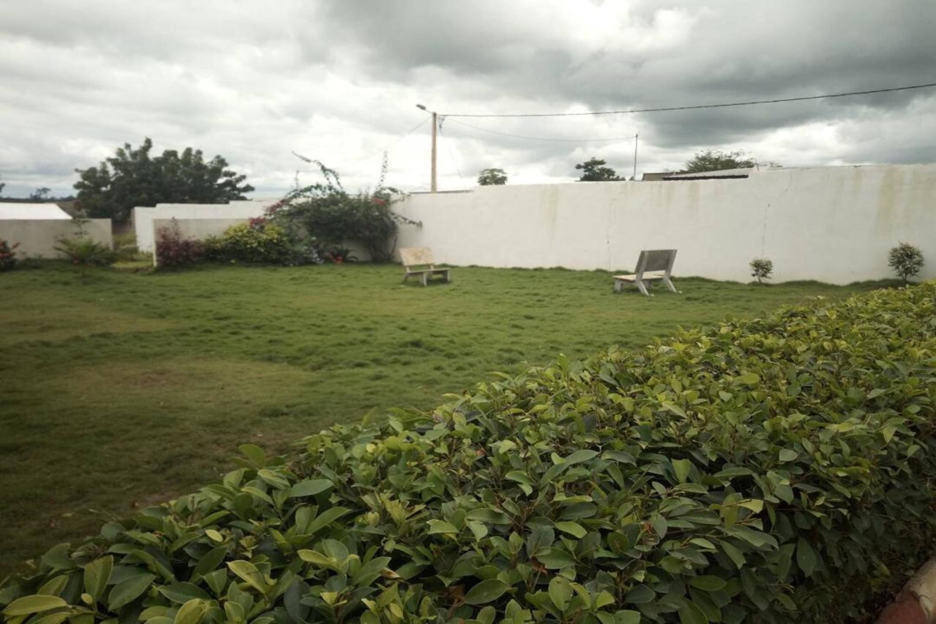 Un patio trasero con césped, una pared blanca, una silla y una pequeña mesa.