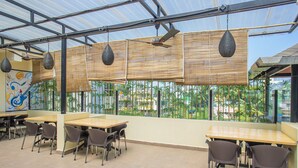 Un restaurant avec des tables et des chaises hautes, un ventilateur de plafond et une vue sur les palmiers à travers de grandes fenêtres.