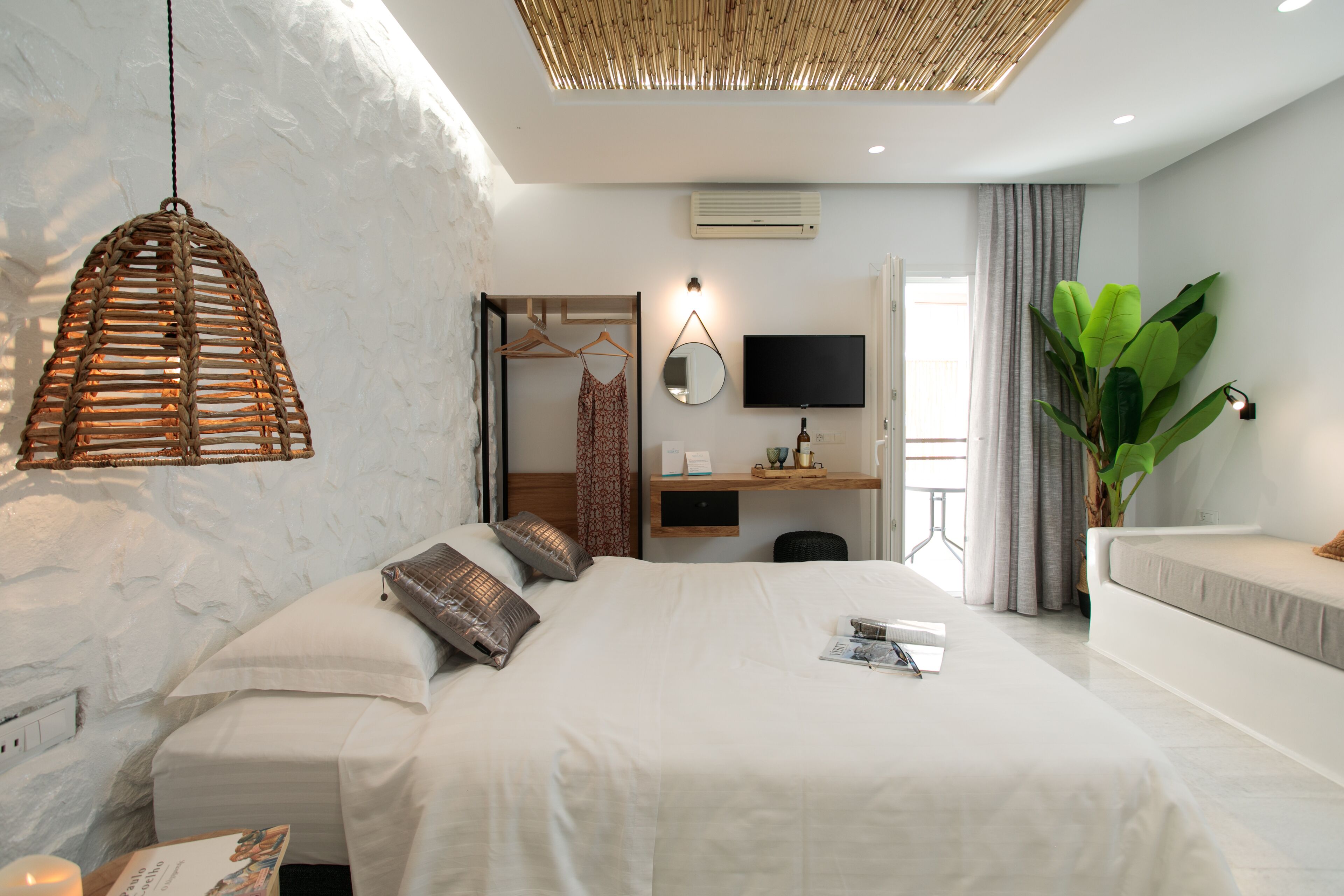 A modern hotel room with a large bed, a desk with a computer, a TV, and a large plant.