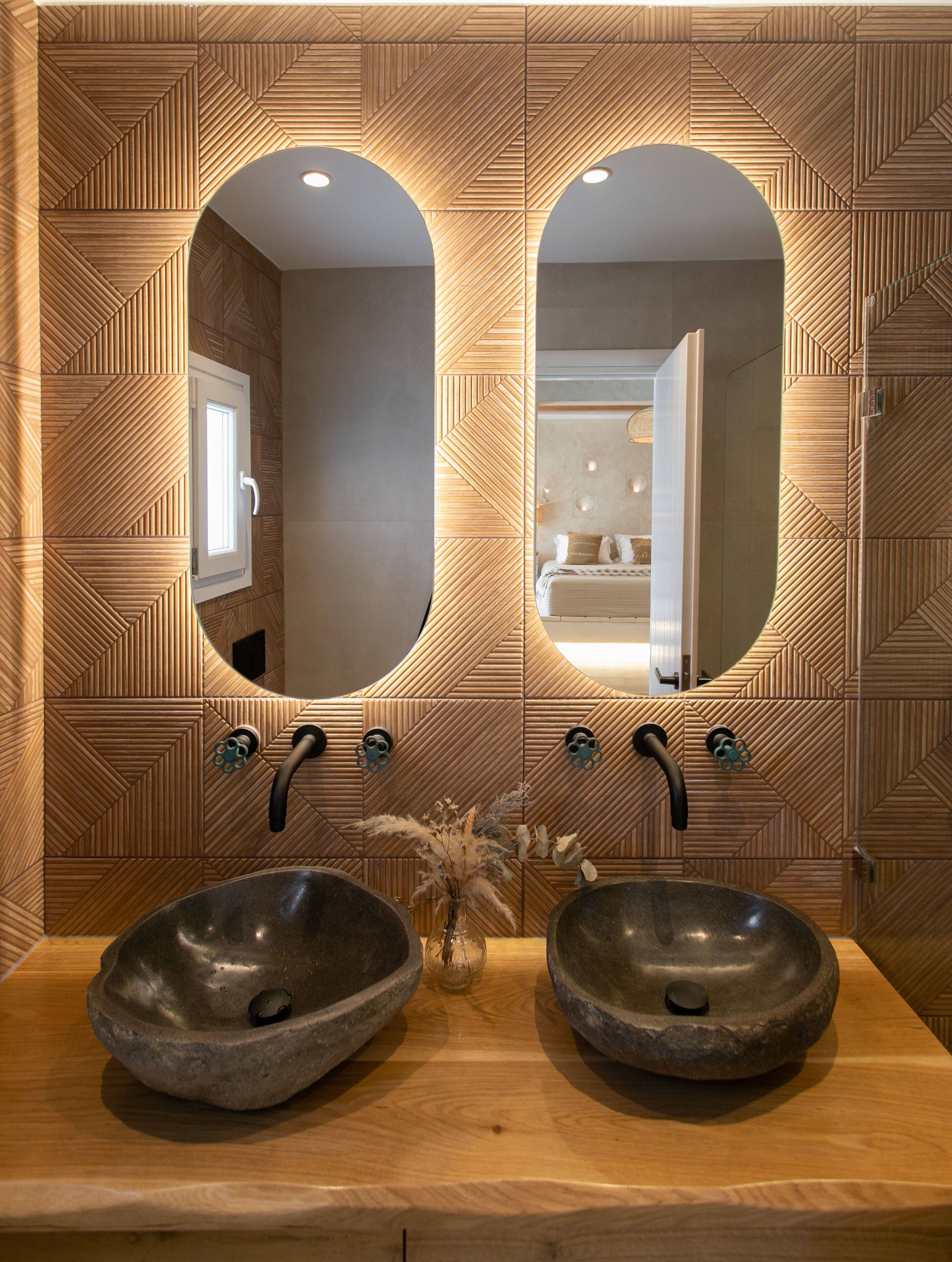 A bathroom with two large oval mirrors, a wooden vanity, and a modern design.