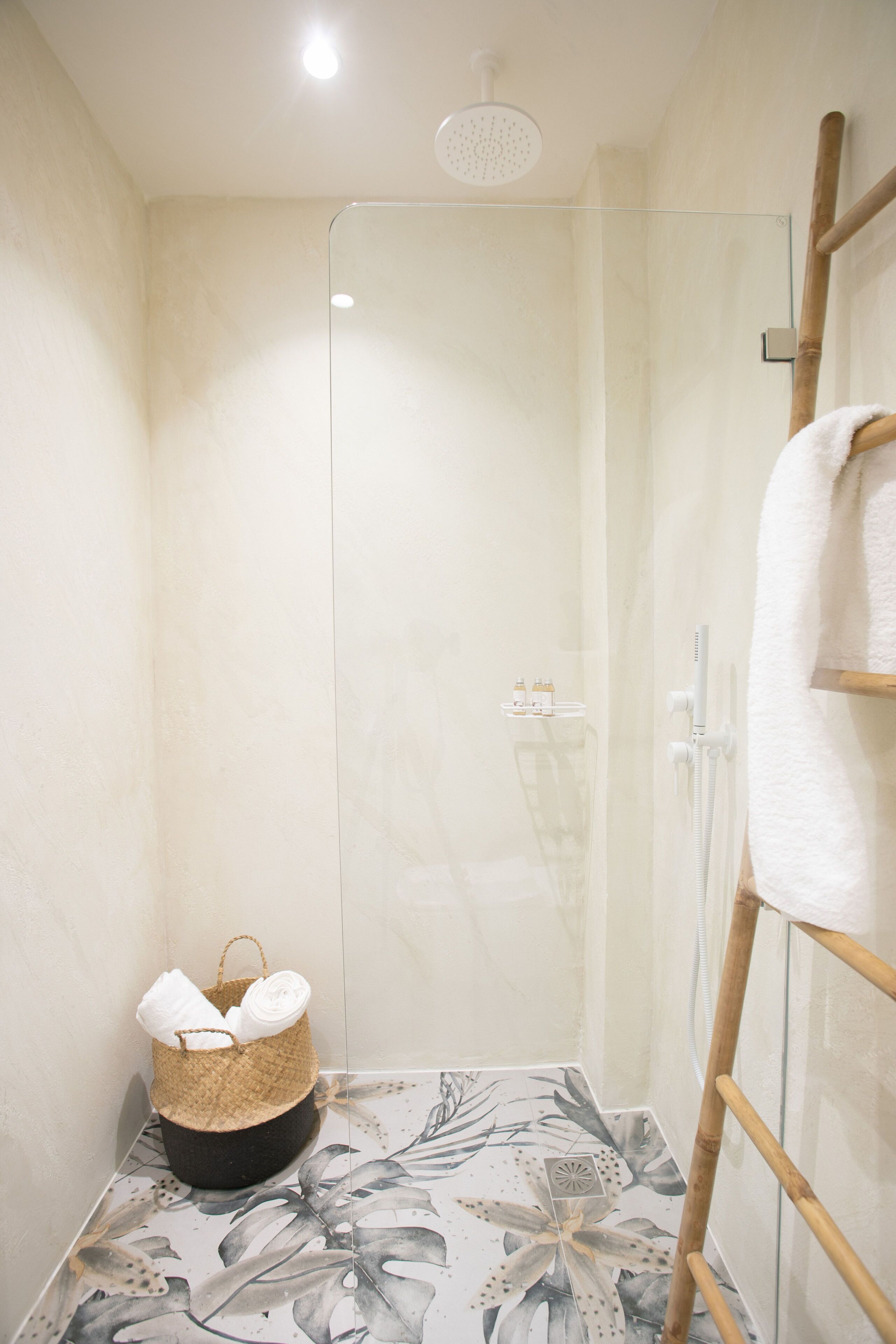 Un espacio de ducha con mampara de vidrio, una escalera de madera y una cesta con toallas.