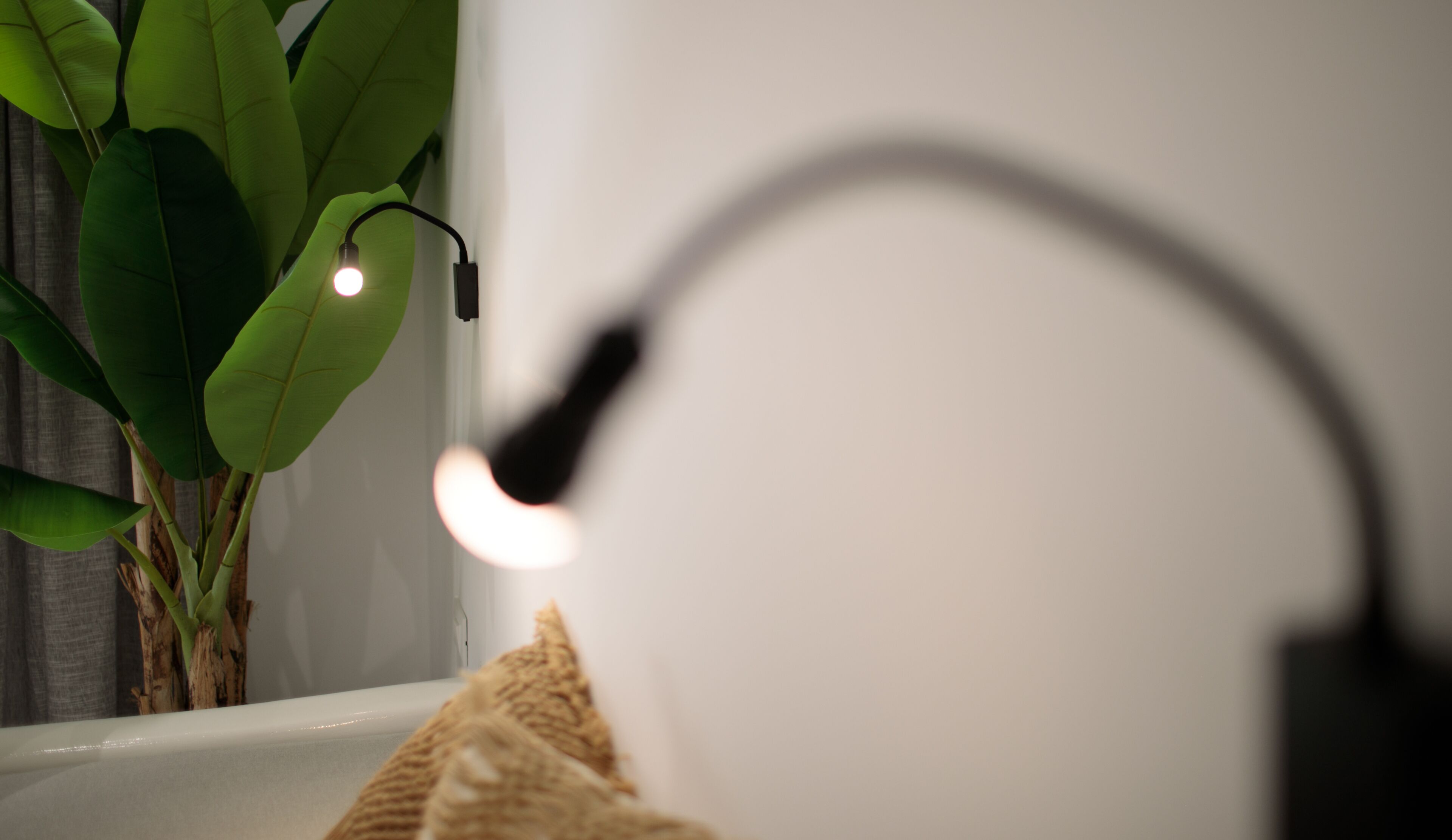 A bathroom with a white bathtub, a black faucet, and a green plant.