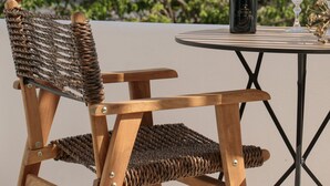 A wooden chair with a woven backrest and a table with a bottle and glasses on it. - Terra Fos Naxos Studios (Naxos)