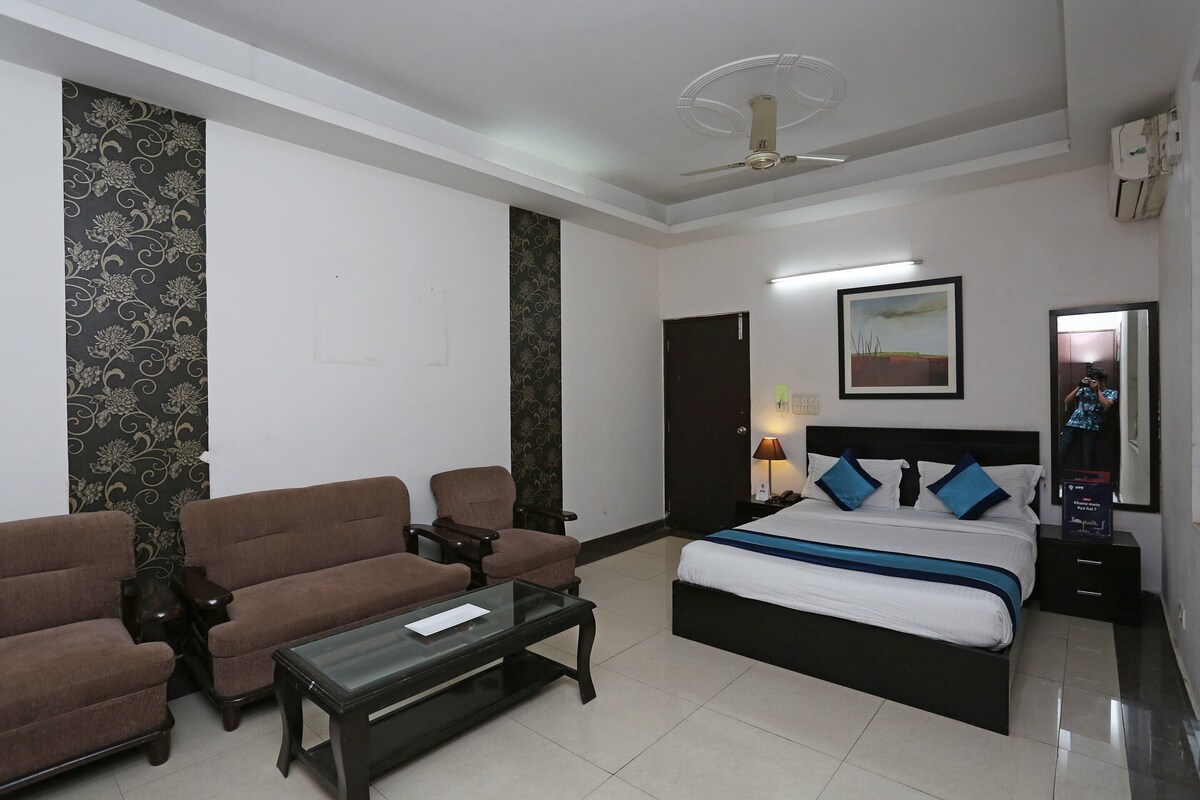 A hotel room with a bed, two brown sofas, a coffee table, a nightstand, a lamp, a ceiling fan, and a framed picture on the wall.
