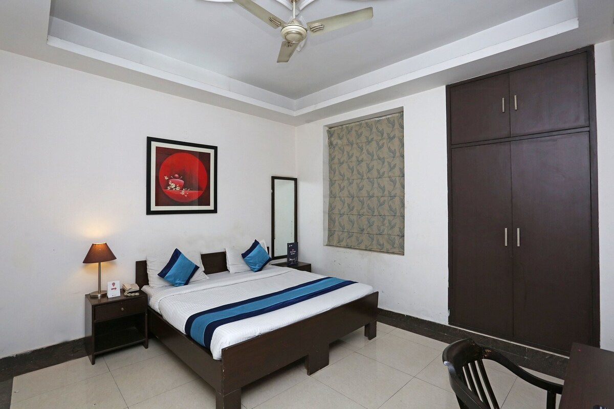 A neatly arranged bedroom with a bed, nightstand, lamp, wardrobe, and a chair.