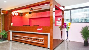 Een receptiebalie in rood en wit, een plafondventilator en een raam met uitzicht op de omgeving.