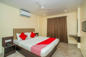 Une chambre d’hôtel équipée d’un lit, d’un ventilateur de plafond, d’un appareil de climatisation, d’une télévision et d’un rideau à motifs.