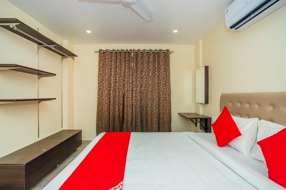 Une chambre d’hôtel comprenant un lit, une table de chevet, une étagère fixée au mur, un ventilateur de plafond et un appareil de climatisation.