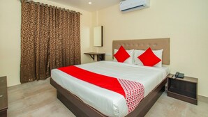 Une chambre d’hôtel avec un grand lit, une table de chevet, un appareil de climatisation et un rideau orné d’un motif géométrique.
