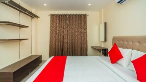 Une chambre d’hôtel avec un lit, une couvre-lit rouge et blanche, un rideau marron à motifs, un ventilateur de plafond et un appareil de climatisation.