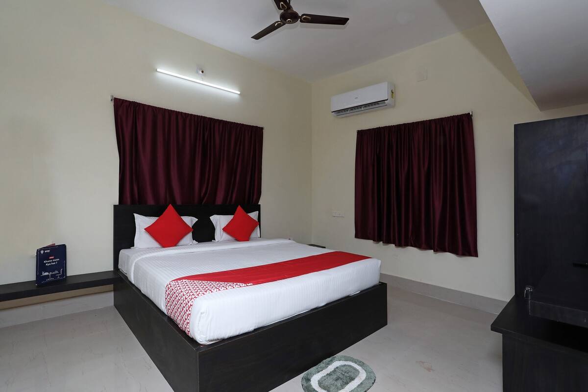 Une chambre à coucher comprenant un lit, des rideaux, un appareil de climatisation, un ventilateur de plafond et un téléviseur.