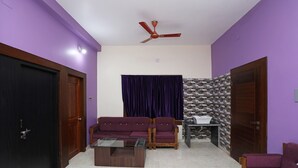 A living room with purple walls, a ceiling fan, a sofa, a coffee table, and a patterned wall. - OYO 16722 The Countryside Resort (Bhubaneshwar)