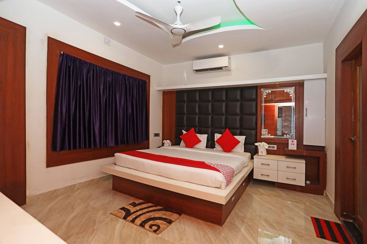 Une chambre moderne avec un grand lit, un ventilateur de plafond, un appareil de climatisation, une coiffeuse avec un miroir et un petit bureau.