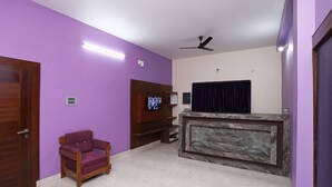A room with purple walls, a wooden chair, a television, a ceiling fan, and a marble floor. - OYO 16722 The Countryside Resort (Bhubaneshwar)