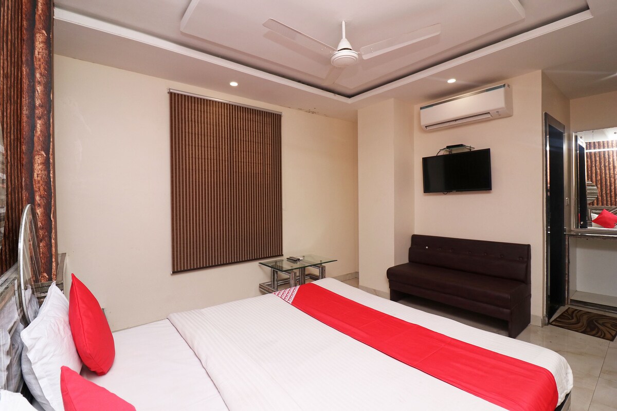 A hotel room with a bed, a sofa, a TV, and a window with blinds.