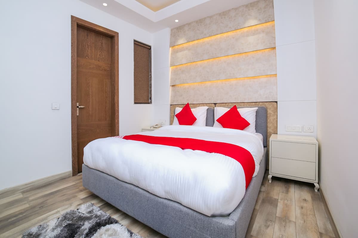 A modern bedroom with a large bed, wooden door, and a nightstand with a lamp.